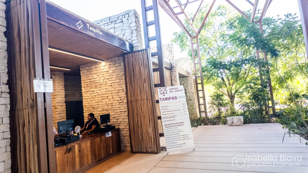 Ticket booth for Parque del Jaguar with a person at the desk, surrounded by stone walls and lush greenery in the background.