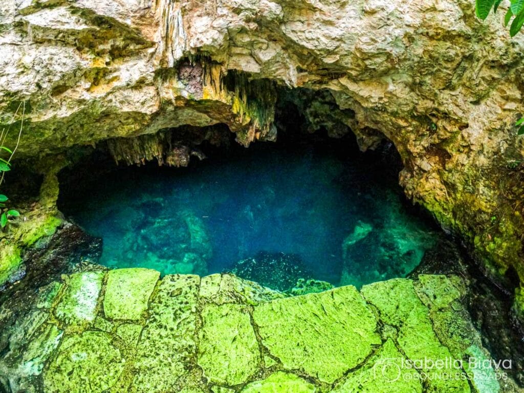 Natural underground cave pool with clear blue water, surrounded by rocky formations. No people are present, creating a serene, untouched atmosphere.